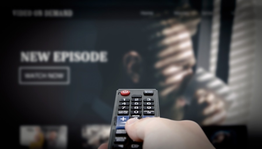 A picture of a hand holding a remote control pointing towards TV screen which says "new episode" onscreen